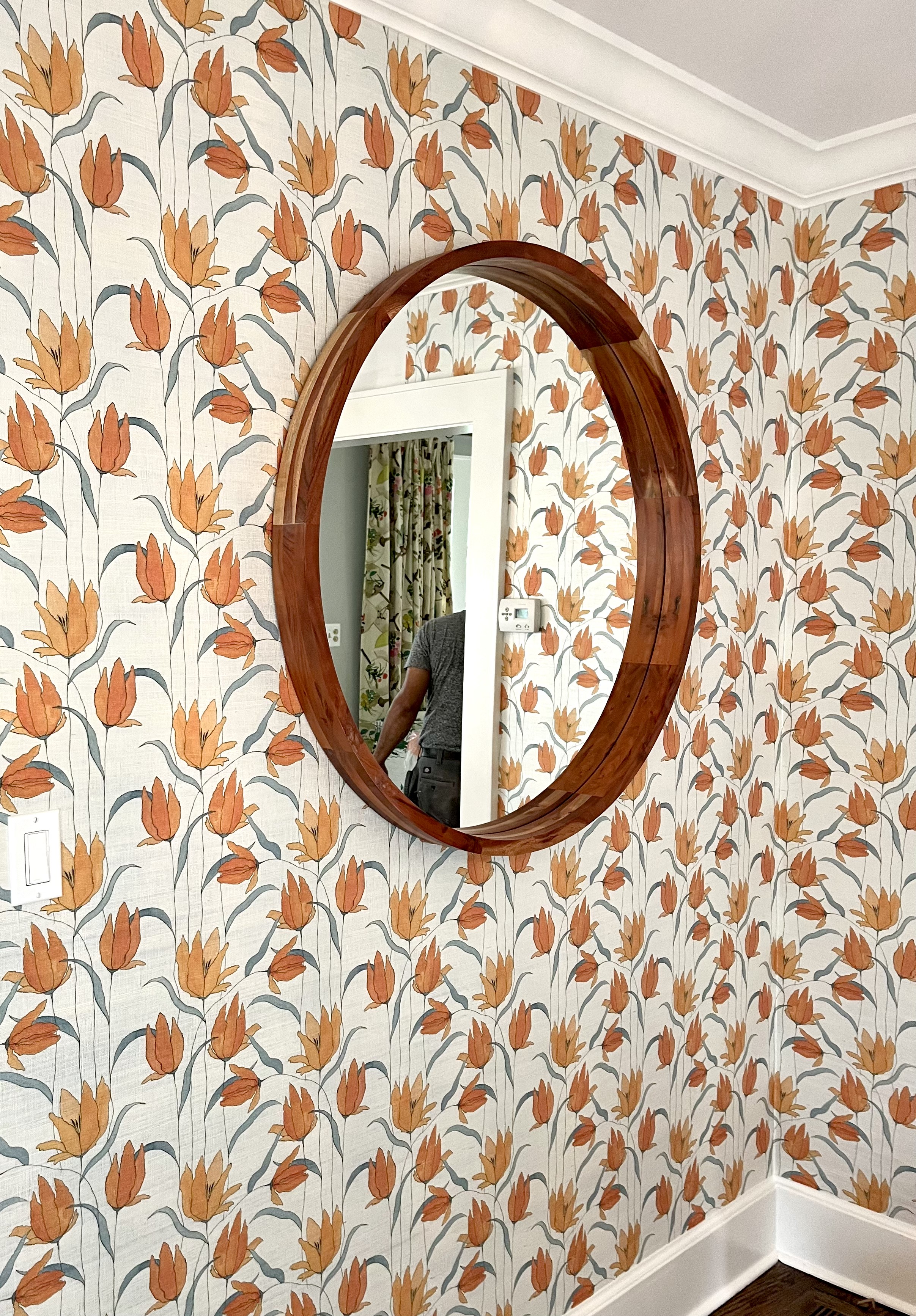 Entryway with orange floral wallpaper and round wooden mirror